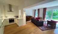 Offene Wohnküche im Apartmenthaus Christina in Nürnberg mit moderner Einbauküche, großzügigem Wohnbereich, Holzboden, stilvollem Mobiliar und Zugang zur grünen Terrasse – perfekte Kombination aus Komfort und Design nahe dem Design Hotel Vosteen. / Open-plan kitchen and living area at Apartmenthaus Christina in Nuremberg featuring a modern fitted kitchen, spacious lounge, wooden flooring, stylish furnishings and access to the green terrace – perfect blend of comfort and design near Design Hotel Vosteen.